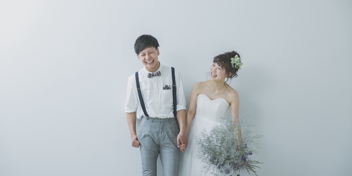 白い壁の前で、手をつないで笑う新郎新婦